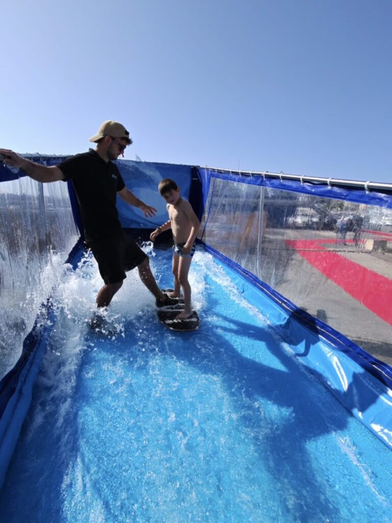 Enfant debout sur la planche sur la vague artificielle, accompagné par un moniteur