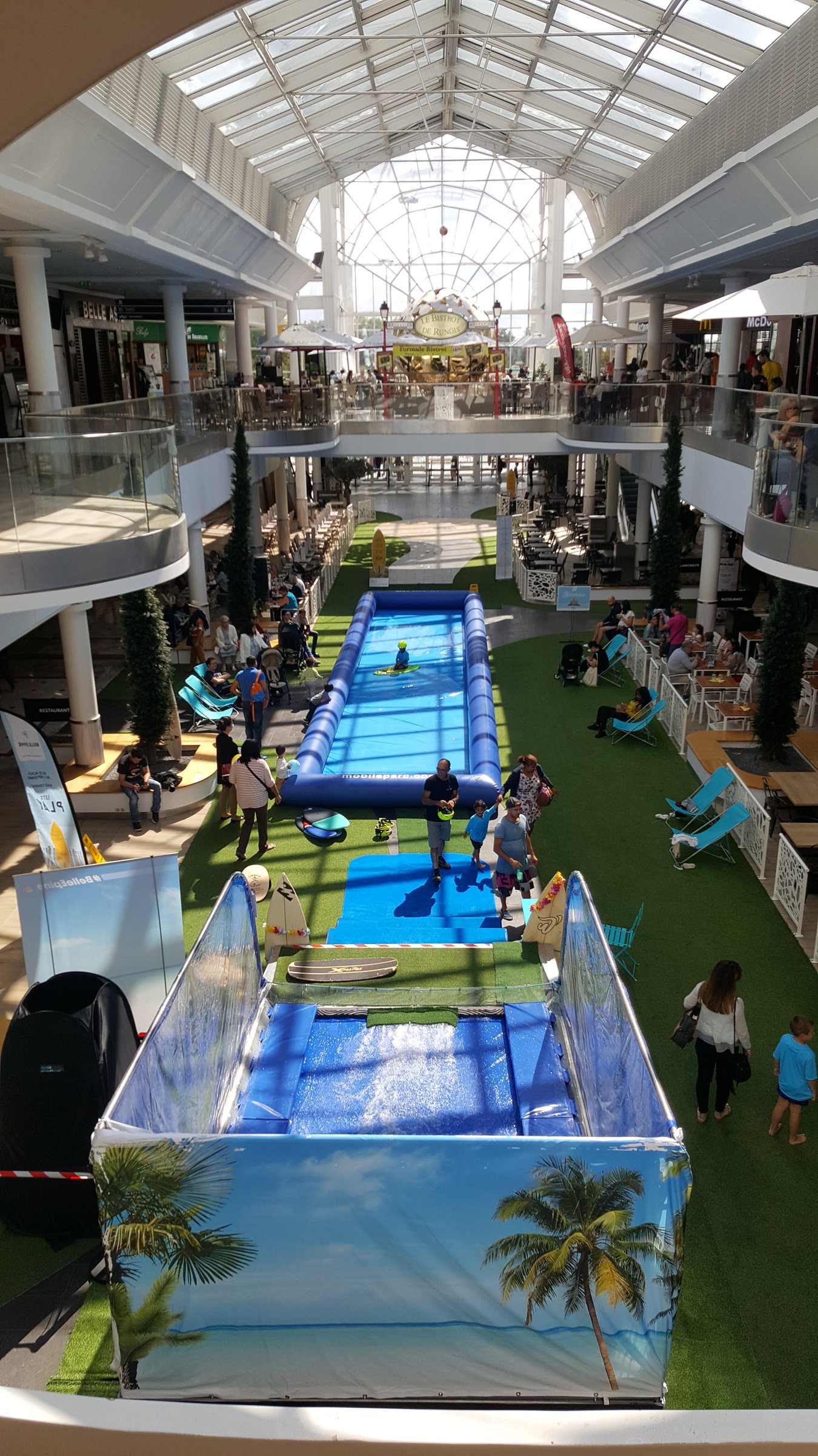 Vue plongeante du GlisssParc installé dans une galerie commerciale, surf au premier plan et bassin de glisse derrière