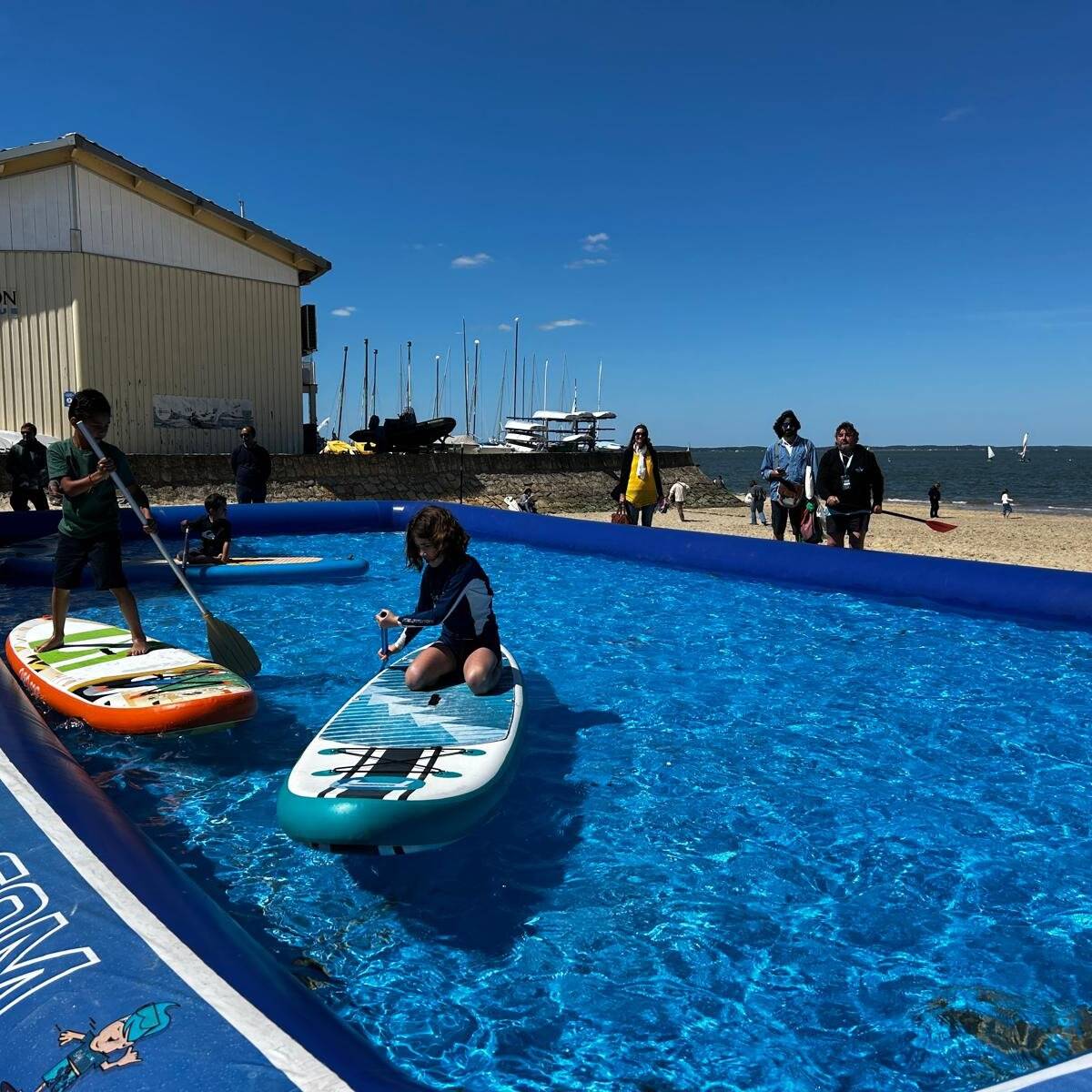 Deux enfants s’initient au stand-up paddle dans le bassin PaddleParc en bord de plage
