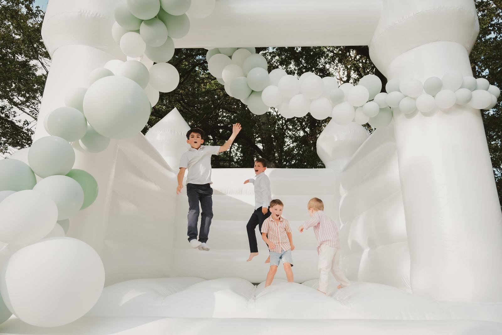 Quatre enfants en tenue de mariage sautent dans le château gonflable blanc