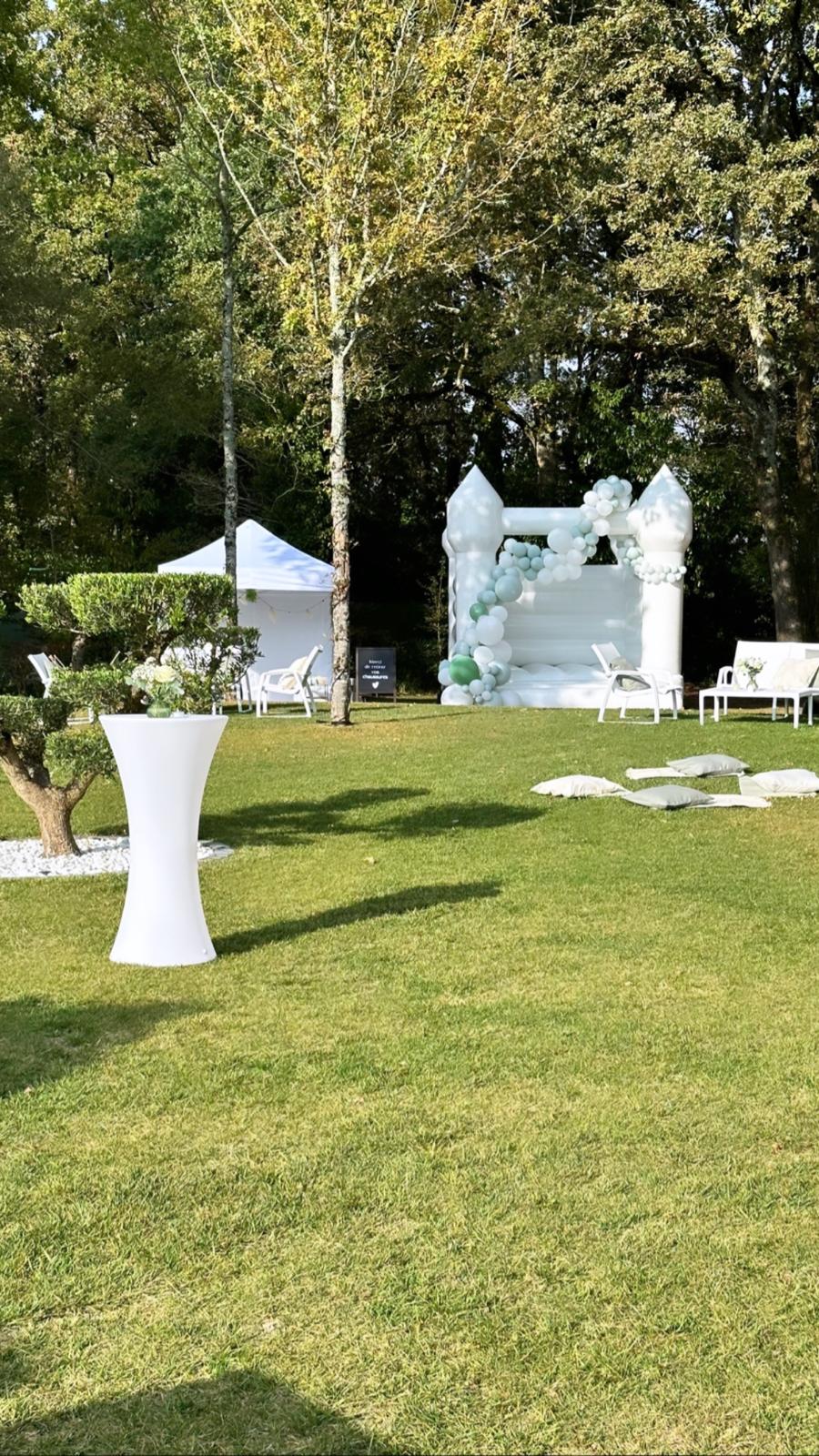 Le château gonflable blanc installé sur la pelouse, près des mange-debout et des transats d'un cocktail