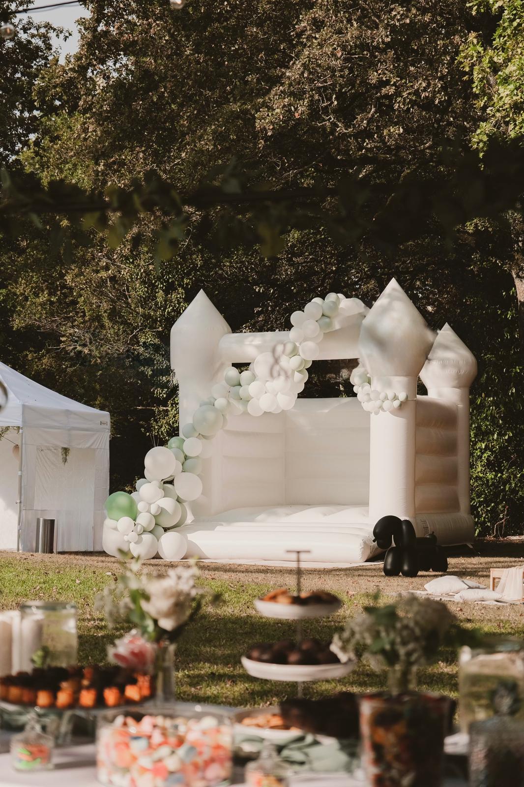 Le château gonflable blanc installé dans un jardin de réception, derrière une table de desserts
