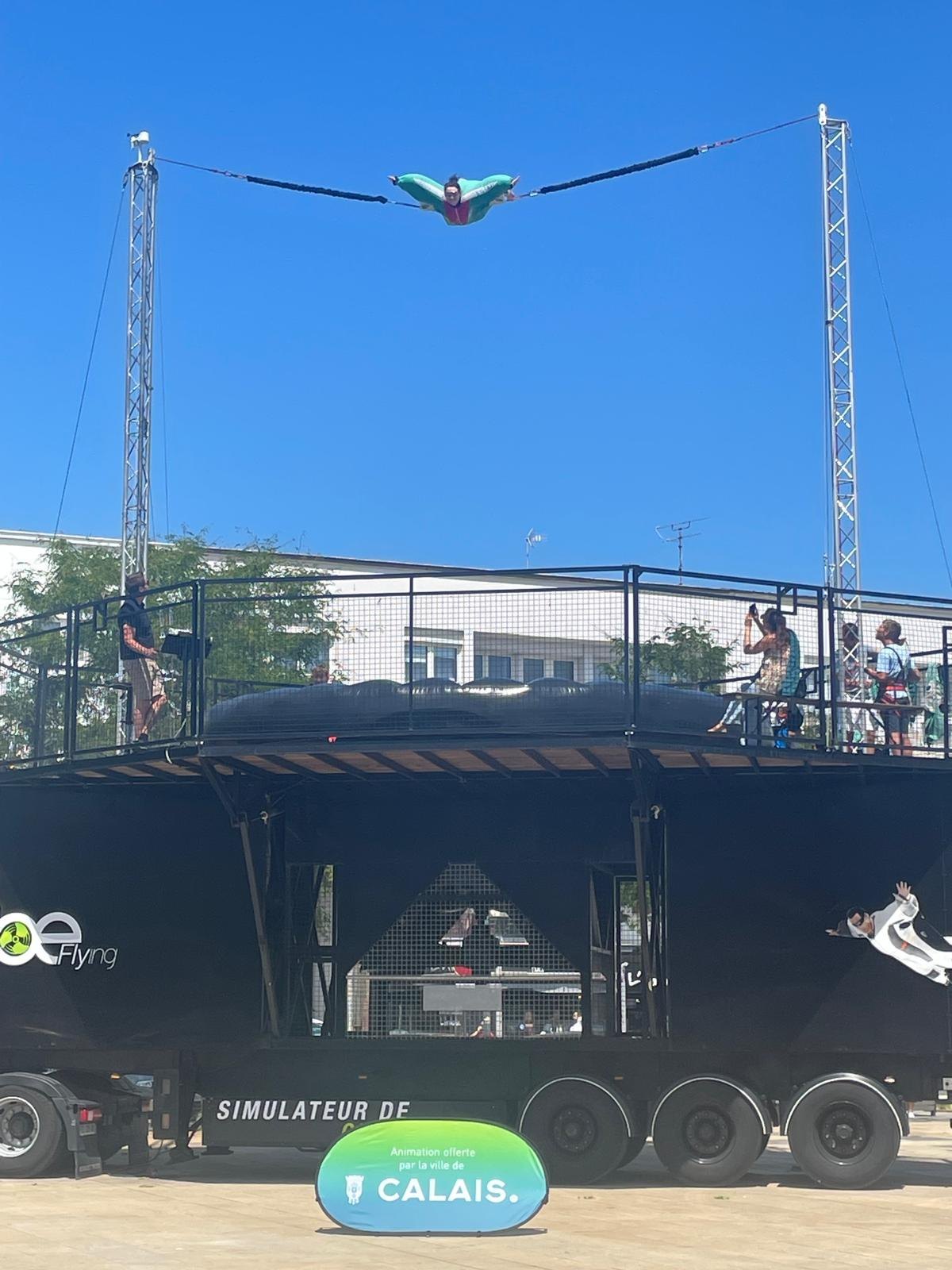 Le simulateur de chute libre sur remorque installé sur une place de Calais, un participant en vol au-dessus de la plateforme