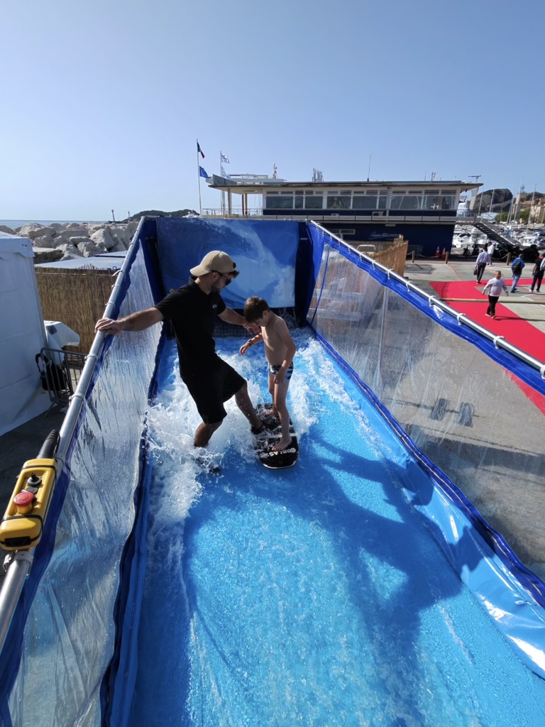 Un moniteur accompagne un enfant sur la vague du simulateur de surf mobile