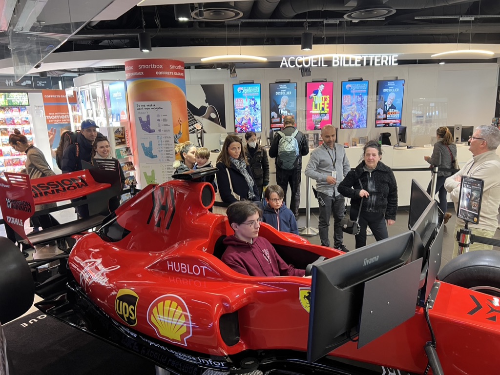 Familles rassemblées autour du simulateur de Formule 1 dans le hall d'accueil d'un centre commercial