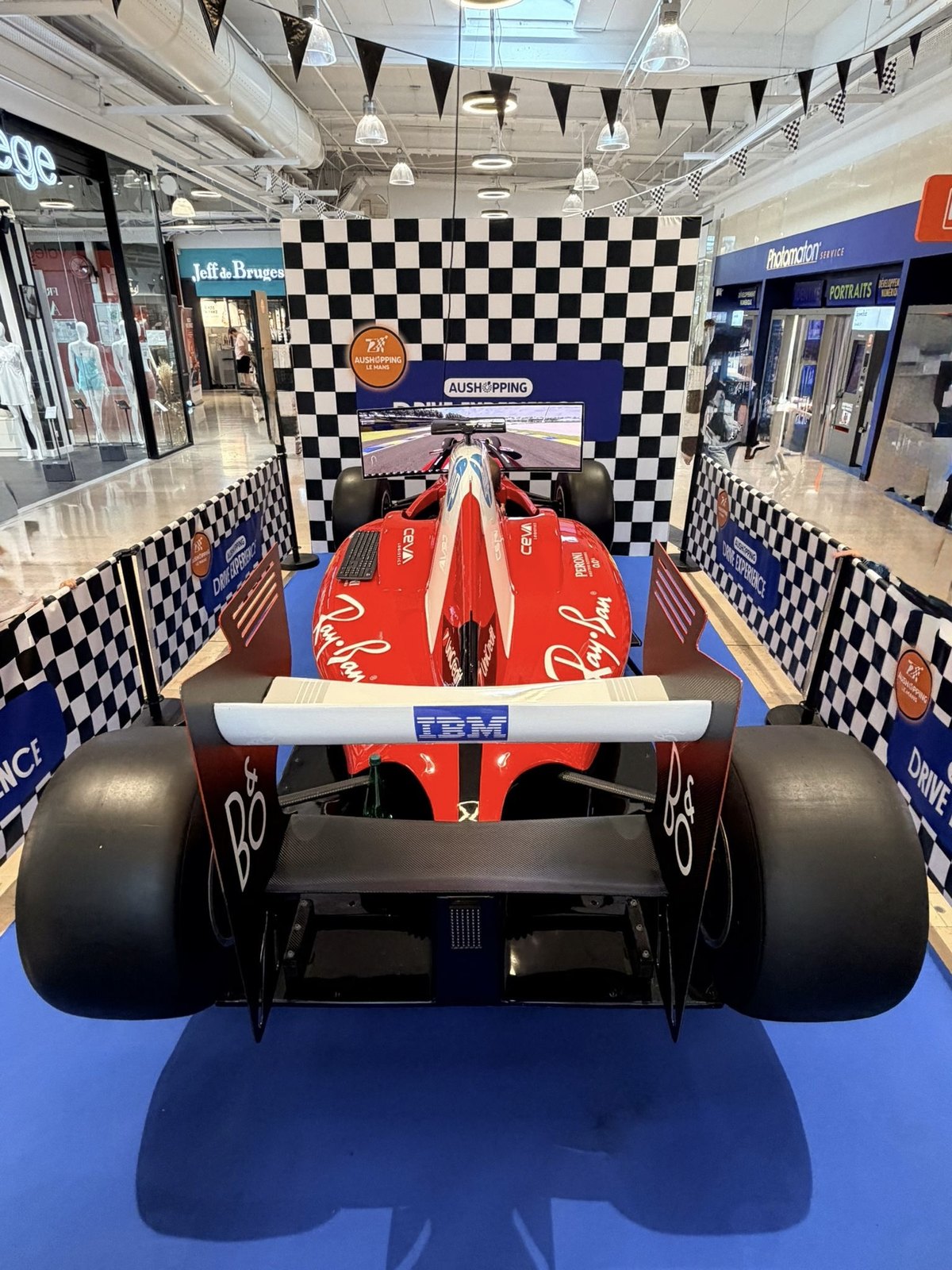 Simulateur de Formule 1 installé dans la galerie du centre commercial Aushopping Le Mans, vu de face avec l'écran de course