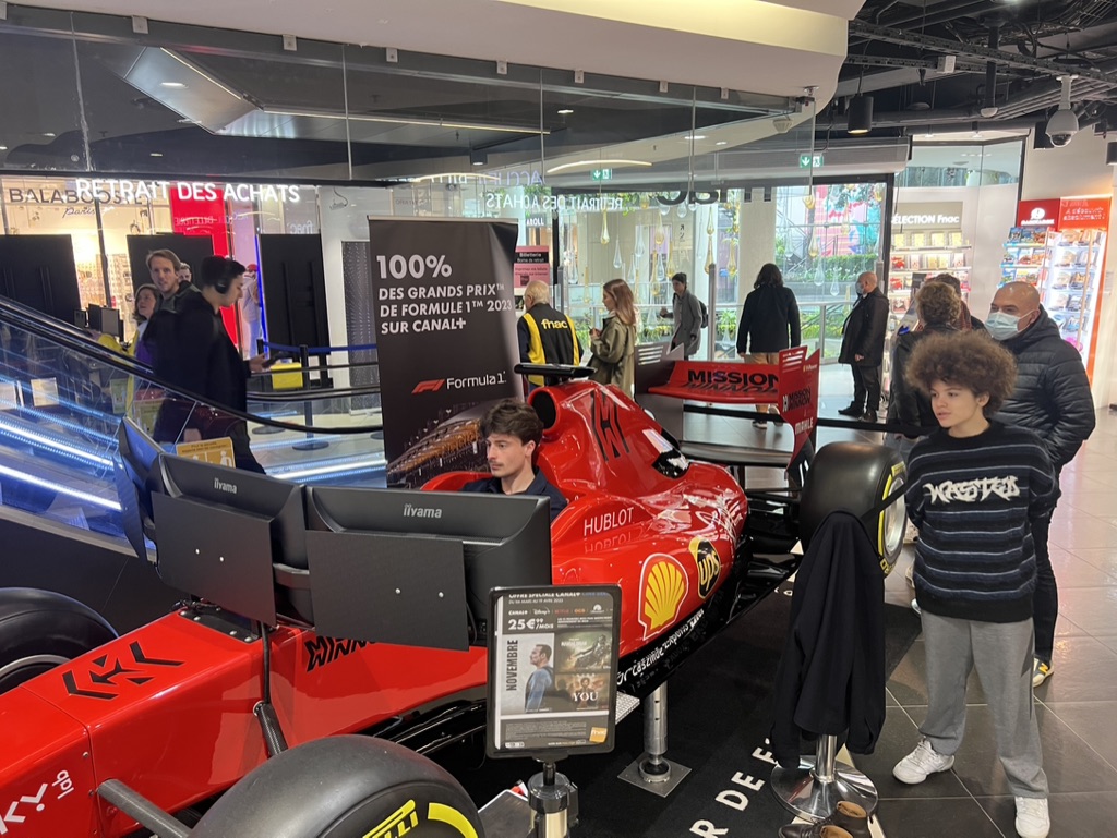 Un visiteur pilote le simulateur de Formule 1 en centre commercial devant le public